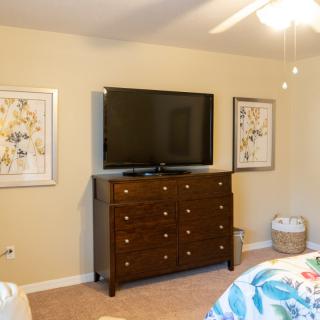 A cozy bedroom with a TV on a dresser and framed artwork on the walls.