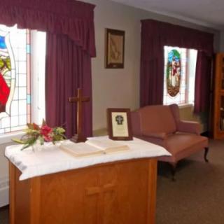 Interior of a chapel featuring an altar with a cross, stained glass windows, and comfortable seating.
