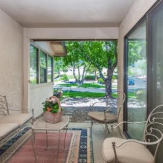 A bright and inviting patio area with modern furniture and large glass windows overlooking a lush, green garden.