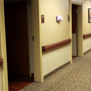A hospital or care facility hallway with open doors and carpeted flooring.
