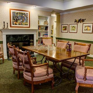 A cozy dining room featuring a wooden table surrounded by upholstered chairs, with artwork on the walls and a fireplace.