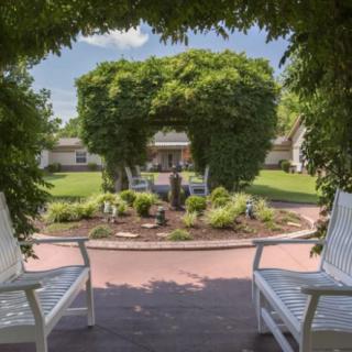 A charming garden view framed by an archway with two white chairs.