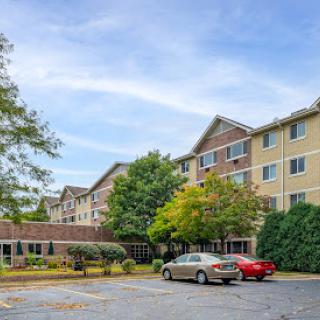 A view of a multi-story residential building with cars parked in front and trees surrounding the area.