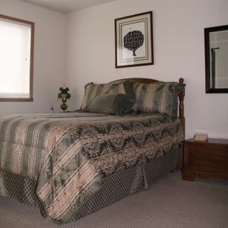 A cozy bedroom featuring a neatly made bed with patterned bedding, artwork on the wall, and a window allowing natural light to fill the room.
