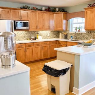 A modern kitchen with wooden cabinets, a microwave, and a trash bin on hardwood flooring.