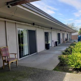 A row of buildings with sliding glass doors opening to a patio area, surrounded by greenery and under a clear blue sky.