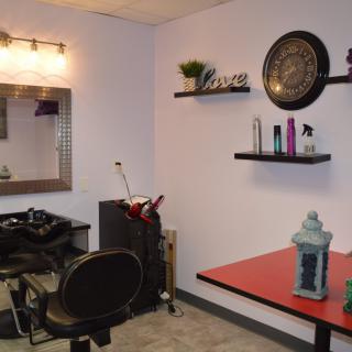 A cozy salon space with styling chair, mirror, and decorative shelves.
