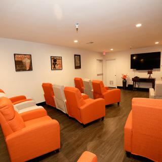 A cozy home theater room featuring orange chairs arranged to face a large television on the wall.