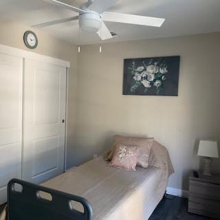 A minimalist bedroom featuring a single bed, a nightstand with a lamp, and a wall painting.