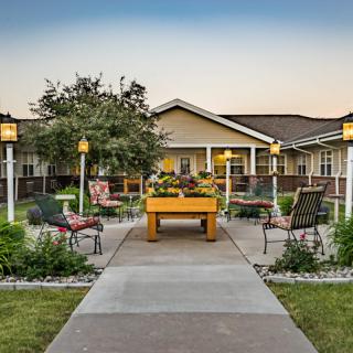 A scenic garden with benches and a pathway leading to a cozy building.