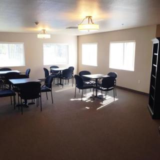 A well-lit room with multiple tables and chairs, featuring large windows and ceiling lights.