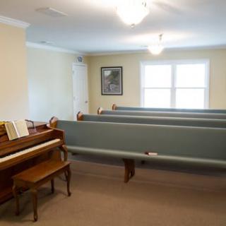 A small chapel interior featuring a piano and rows of benches.