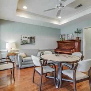 A cozy living room with a sofa, chairs, and a piano, featuring hardwood floors and tasteful artwork.