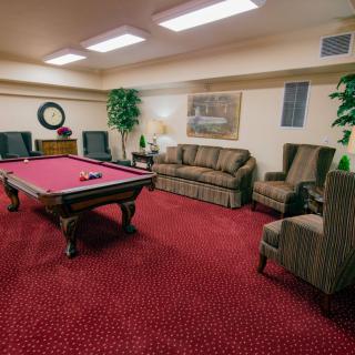 A cozy game room featuring a red pool table surrounded by comfortable seating and lush decorations.