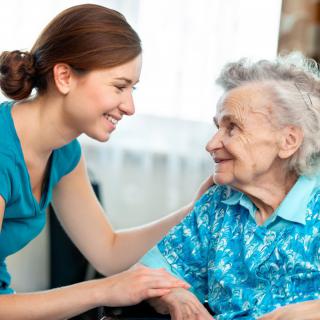 A caregiver smiles warmly at an elderly woman, showing support and companionship.