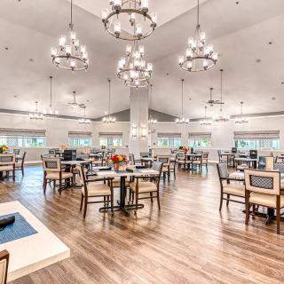A spacious dining room with elegant chandeliers, wooden flooring, and neatly arranged tables and chairs.