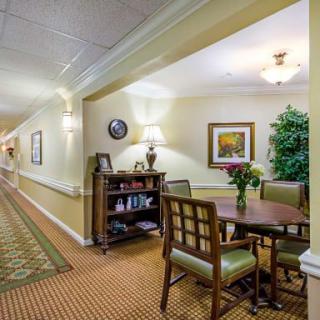 A well-lit hallway with a cozy seating area, featuring a table and chairs, decorated with artwork and plants.
