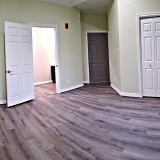 An unfurnished room with hardwood floors, light-colored walls, and several doors.
