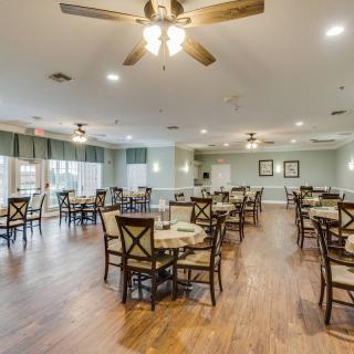 A spacious dining area with wooden floors, multiple tables and chairs, and ceiling fans.