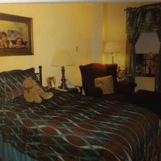 A cozy bedroom with a well-decorated bed, featuring patterned bedding, lamps, armchair, and curtain accents.