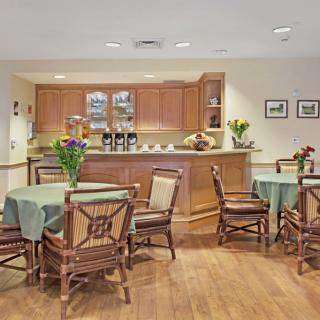 A cozy dining area with several tables and chairs, featuring a kitchenette in the background.