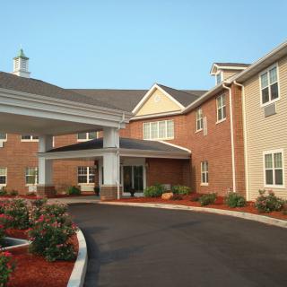 A modern residential building with a covered entrance and landscaped driveway.
