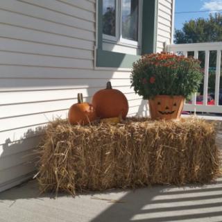 A cozy autumn-themed porch display with pumpkins and a hay bale.