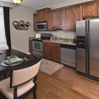 A modern kitchen with wooden cabinets and stainless steel appliances, adjacent to a small dining area with hardwood floors.