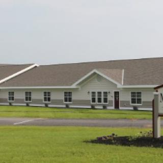 A single-story institutional building with a well-maintained lawn and clear sky.