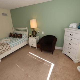 A cozy bedroom with a single bed, nightstand, lamp, armchair, and dresser.