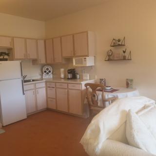 A cozy apartment kitchen with wooden cabinets, a fridge, microwave, and dining area.