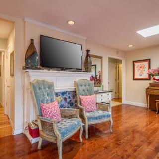 A cozy living room with comfortable chairs, a television mounted above the fireplace, and elegant decor.