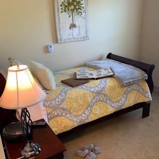 A cozy bedroom with a neatly arranged bed, bedside lamp, and artwork on the wall.