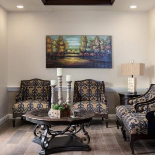 A cozy living room with patterned chairs, a central coffee table, and a colorful painting on the wall.