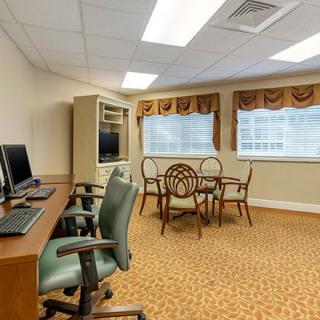 A well-lit office space featuring computers on desks and a round table with chairs near windows.