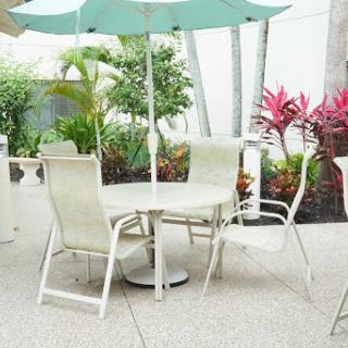 A cozy outdoor seating area with a table, chairs, and an umbrella surrounded by vibrant plants.