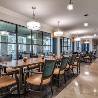 A modern dining area with a long wooden table, surrounded by chairs and illuminated by pendant lights.