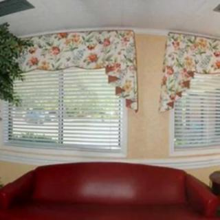 A cozy living room with a red sofa, floral-patterned curtains, and large windows with blinds.