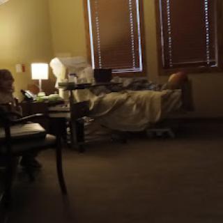 A hospital room featuring a patient in bed and a caregiver sitting nearby.