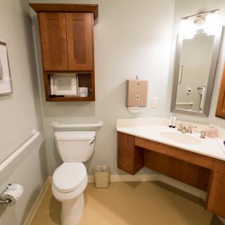 A clean and functional bathroom with a toilet, sink, mirror, and wooden cabinetry.