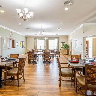 A spacious dining room with wooden floors, multiple tables and chairs, and elegant chandeliers.