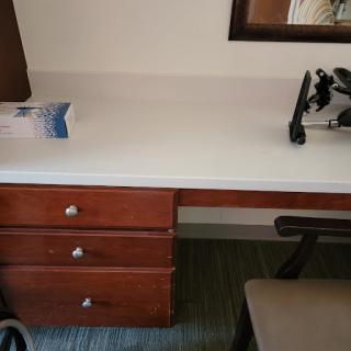 A tidy workspace featuring a wooden desk with three drawers, a chair, and some office supplies.