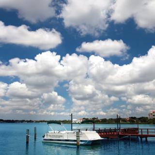 A serene view of a boat docked at a pier under a sky filled with fluffy clouds.