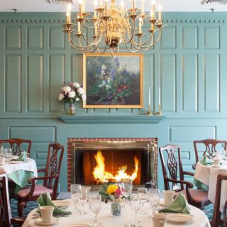 A formal dining room featuring a lit fireplace, an ornate chandelier, and elegantly set tables.