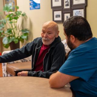 An elderly man engages in a thoughtful conversation with a caregiver in a cozy indoor setting.