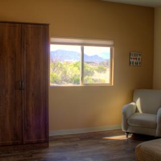 A cozy room with a window showcasing mountain views, featuring simple furniture and warm tones.
