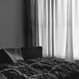 A serene black and white depiction of a bedroom with soft curtains filtering light.