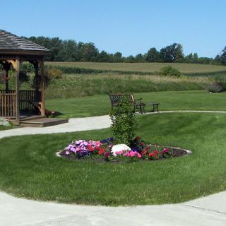 A picturesque garden featuring a gazebo, colorful flowers, and a well-manicured lawn under a clear blue sky.