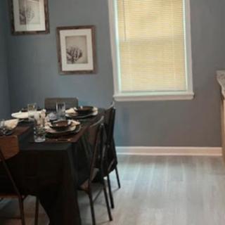 A cozy dining room with a table set for a meal, featuring dark tableware and framed artwork on the walls.