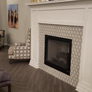 A modern living room features a stylish fireplace with a patterned tile surround, accompanied by a patterned chair and wall artwork.